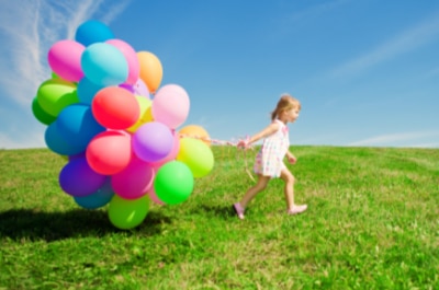 Kind mit bunten Luftballons auf grüner Wiese