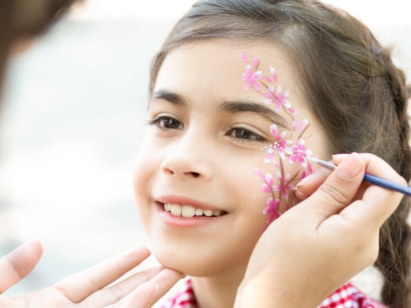 Kinderschminken - ein Kind bekommt ein Blumenmotiv geschminkt